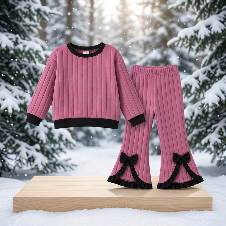 Dusty-pink ribbed top and black bow-detail flared trousers on a wooden platform with snowy evergreen trees behind