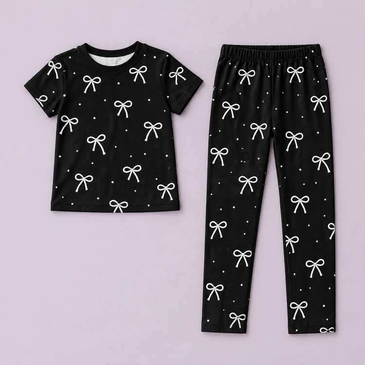 Black bow-print short sleeve top and matching pants laid out on a dusty lilac background without a model